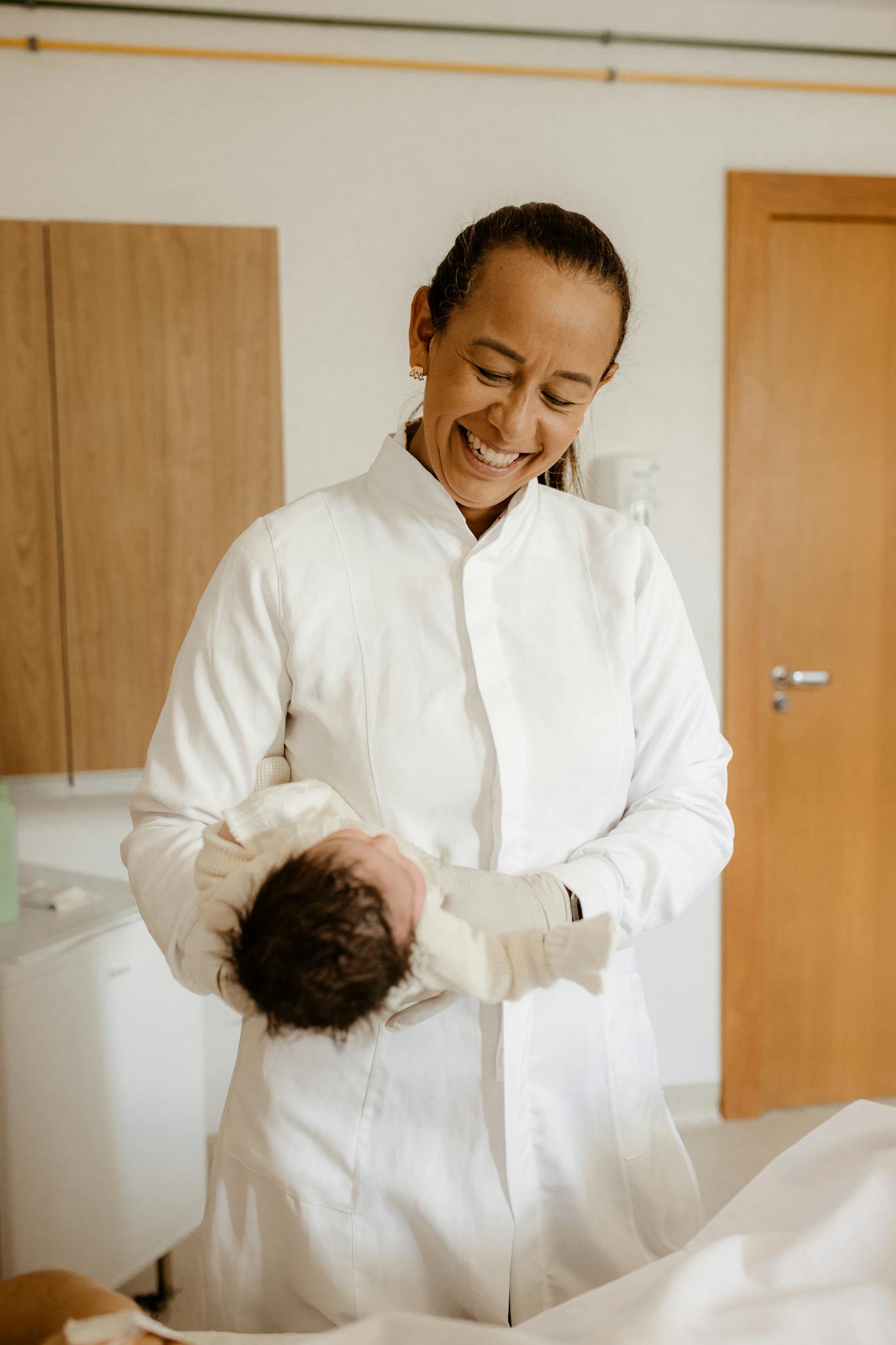 Home 5 A joyful female doctor cradles a newborn baby indoors at a hospital.