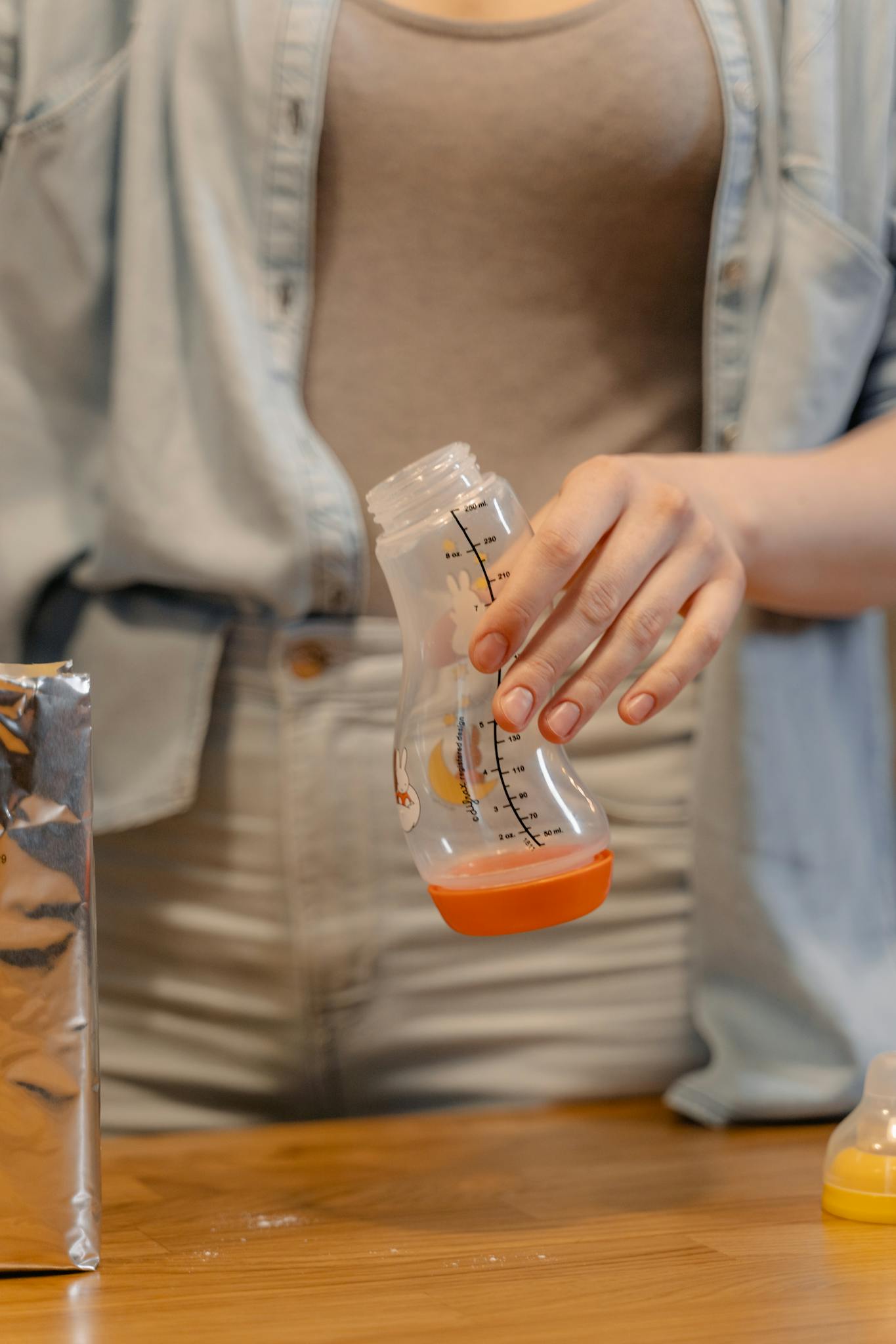 A person preparing a baby bottle with infant formula indoors in a casual setting.